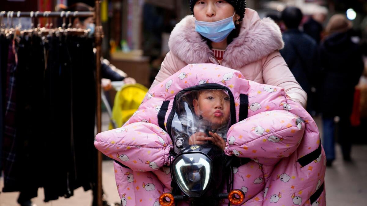 A woman wearing a face mask rides a bicycle with a child, following an outbreak of the coronavirus disease in Wuhan, Hubei province, China.