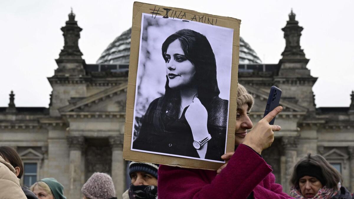 An woman takes a selfie as she holds a portrait of Mahsa Amini, a young Iranian woman who died after being arrested in Tehran by the  morality police, during a demonstration in front of the German lower house of parliament (Bundestag), on  on March 8, 2023. --- AFP file