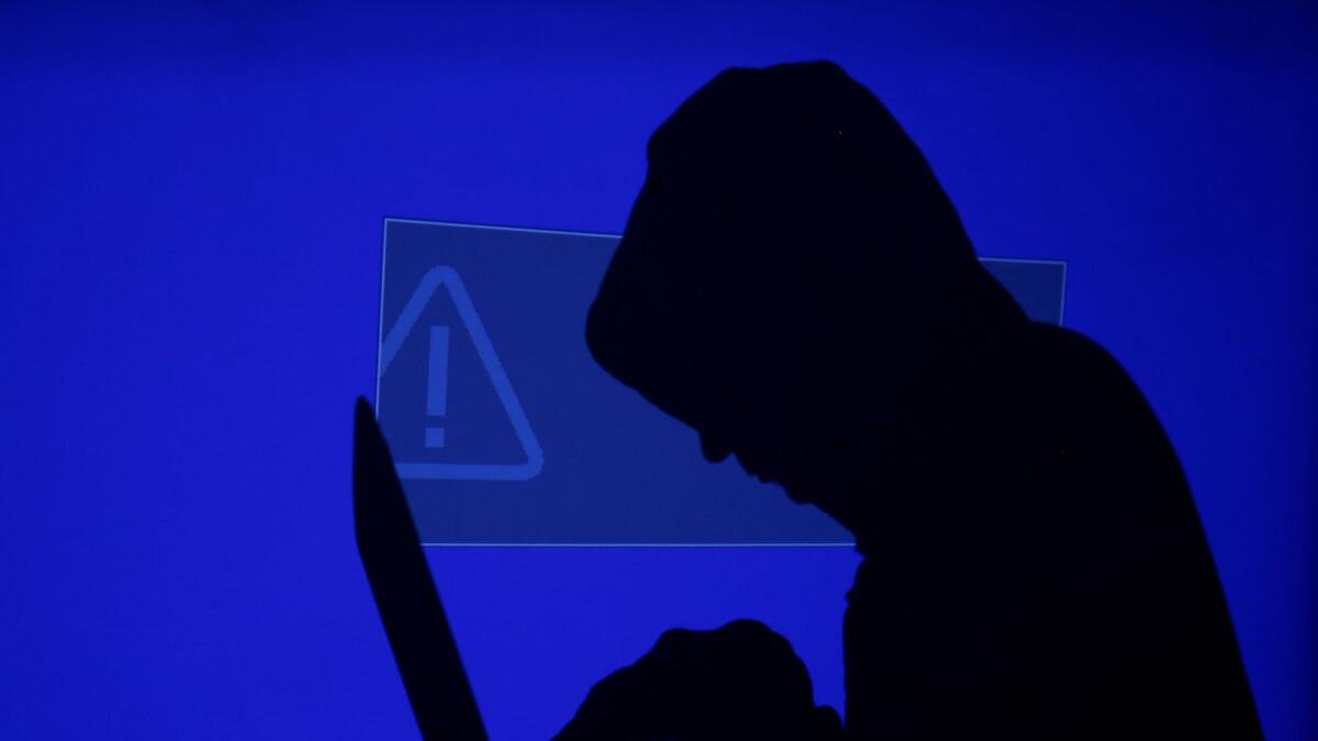 A hooded man holds a laptop computer as blue screen with an exclamation mark is projected on him in this illustration picture taken on May 13, 2017.