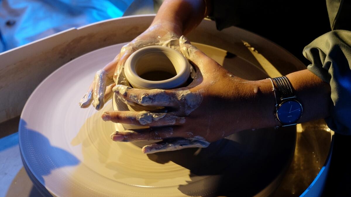 A woman potter molds bowl from clay on the pottery wheel at the event.