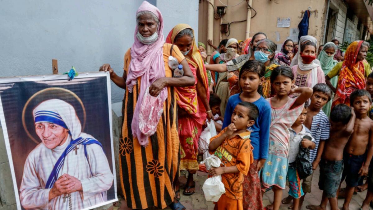 Homeless people gather beside a portrait of Mother Teresa, the founder of the Missionaries of Charity, to collect free food outside the order's headquarters in Kolkata. — AP file