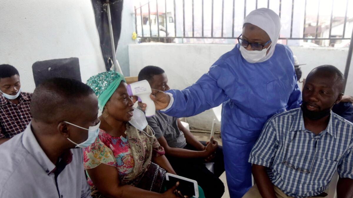 A nurse in protective gear takes temperature of people waiting to take the Covid-19 vaccine at the health centre in Lagos. — AP