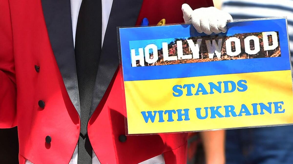 Self-proclaimed Hollywood ambassador Gregg Donovan holds a miniature replica of the Academy Award and a placard showing support for Ukraine. (AFP)
