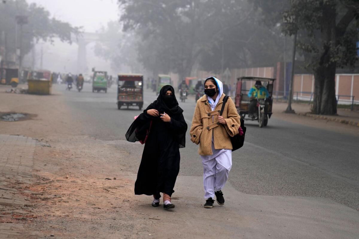 Students, wearing masks, walk towards their college as smog envelops the area, in Lahore, Pakistan, on January 15, 2024. — AP