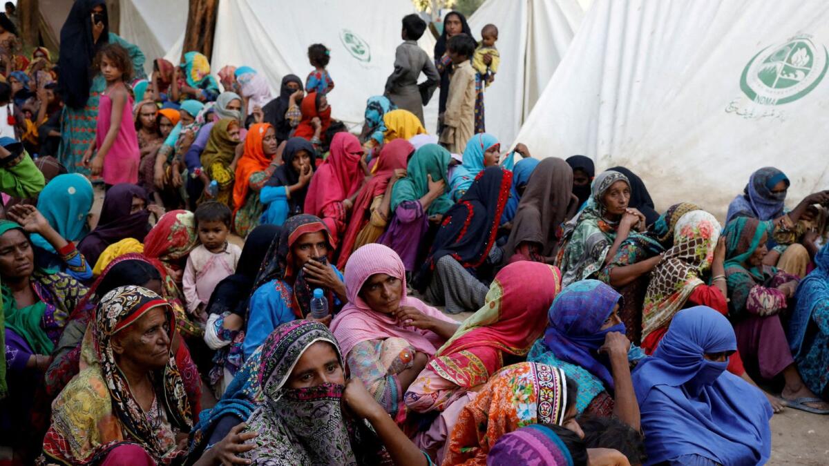 Women displaced because of the floods wait to receive food handouts while taking refuge in a camp, in Sehwan, Pakistan. — Reuters file