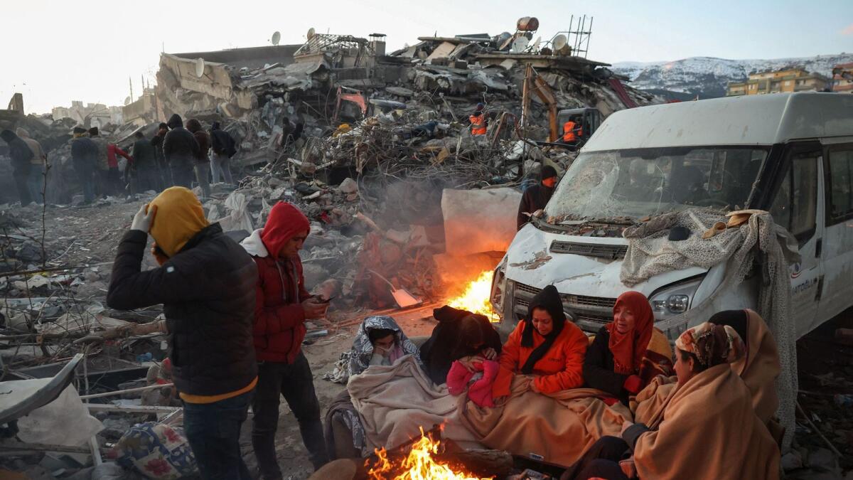 Survivors gather next to a bonfire outside collapsed buildings in Kahramanmaras on February 8, after their homes were destroyed in the catastrophic earthquake. —AFP