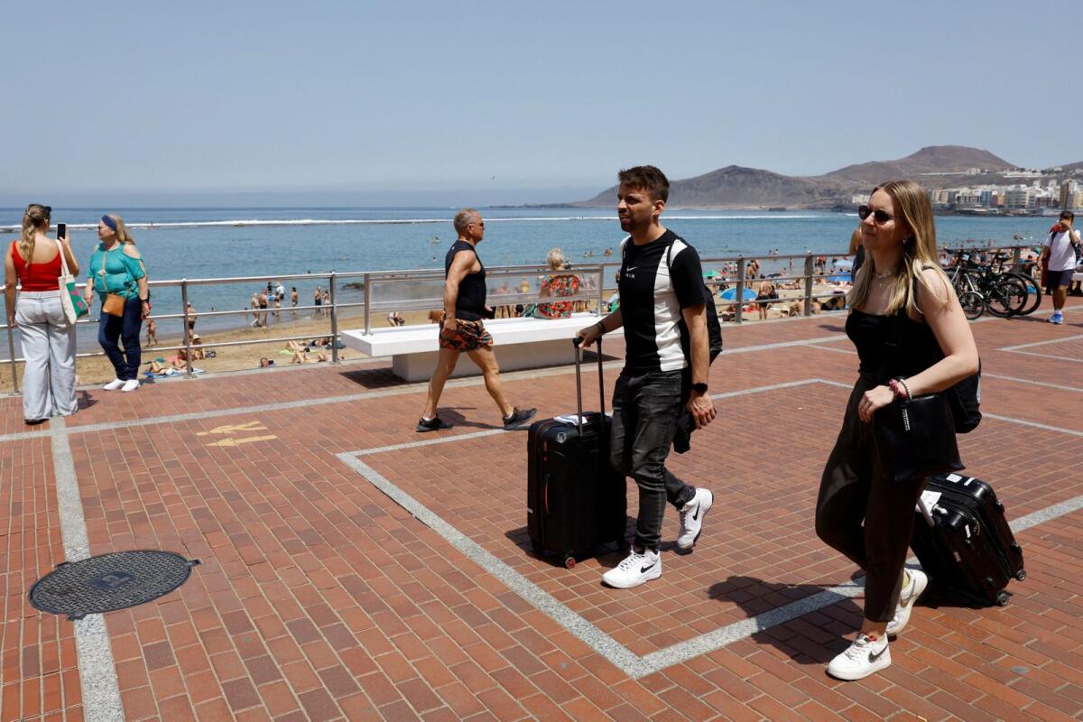 A tourist couple walk with their travel suitcases along the promenade of Las Canteras Beach in Las Palmas de Gran Canaria, Spain, on April 13, 2024. — Reuters