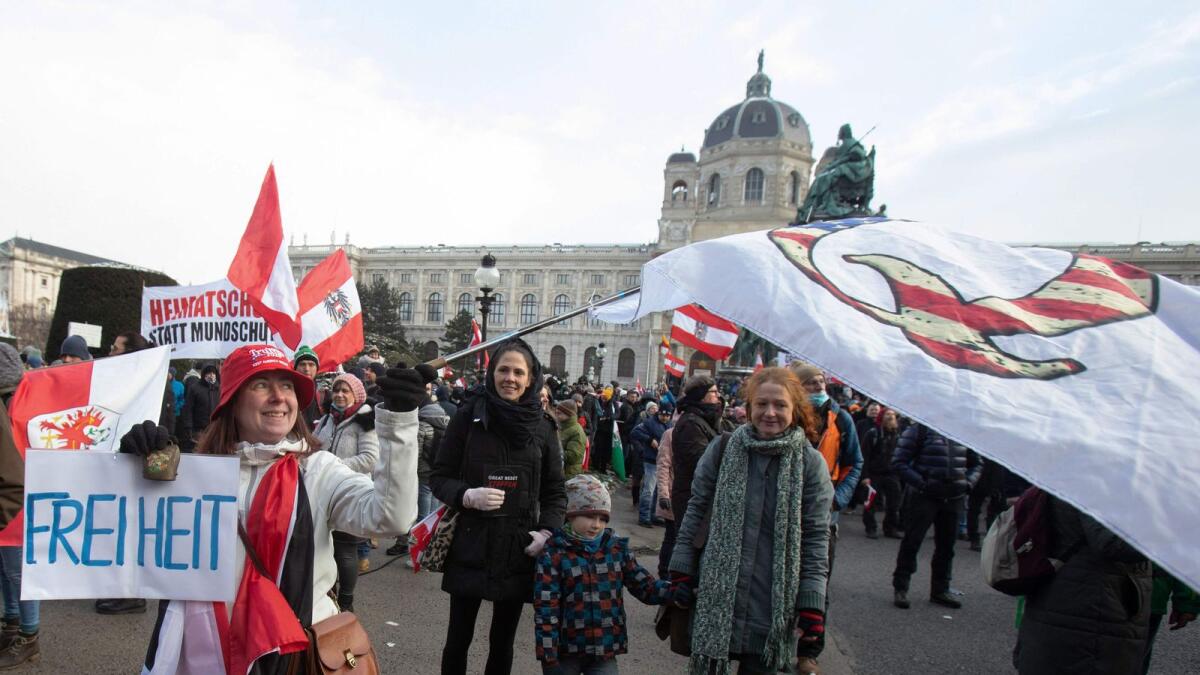 A demonstrator holds a QAnon flag and a poster reading 'Freedom' during a protest against the novel coronavirus (Covid-19) restrictions at the Maria Theresien Platz in Vienna, Austria.