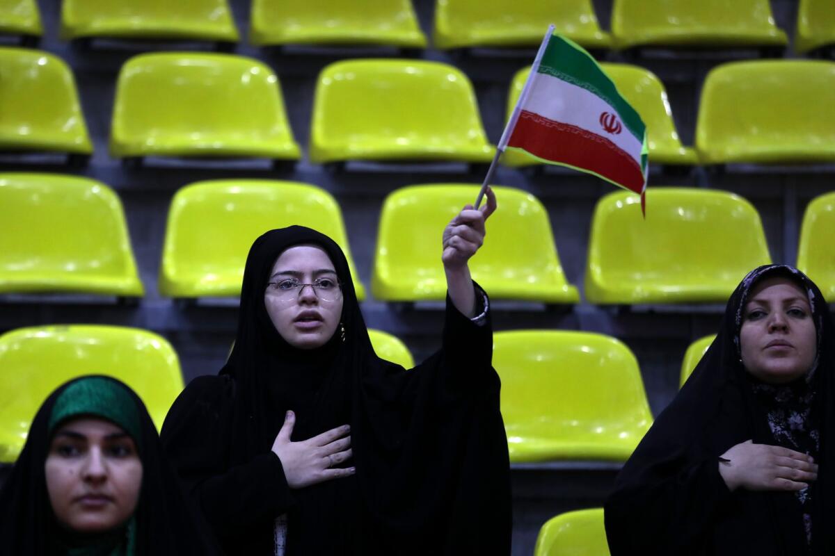 Iranian women listen to their country's national anthem as one of them waves the national flag during an election campaign rally ahead of the March 1, parliamentary and Assembly of Experts elections in Tehran on Tuesday. — AP