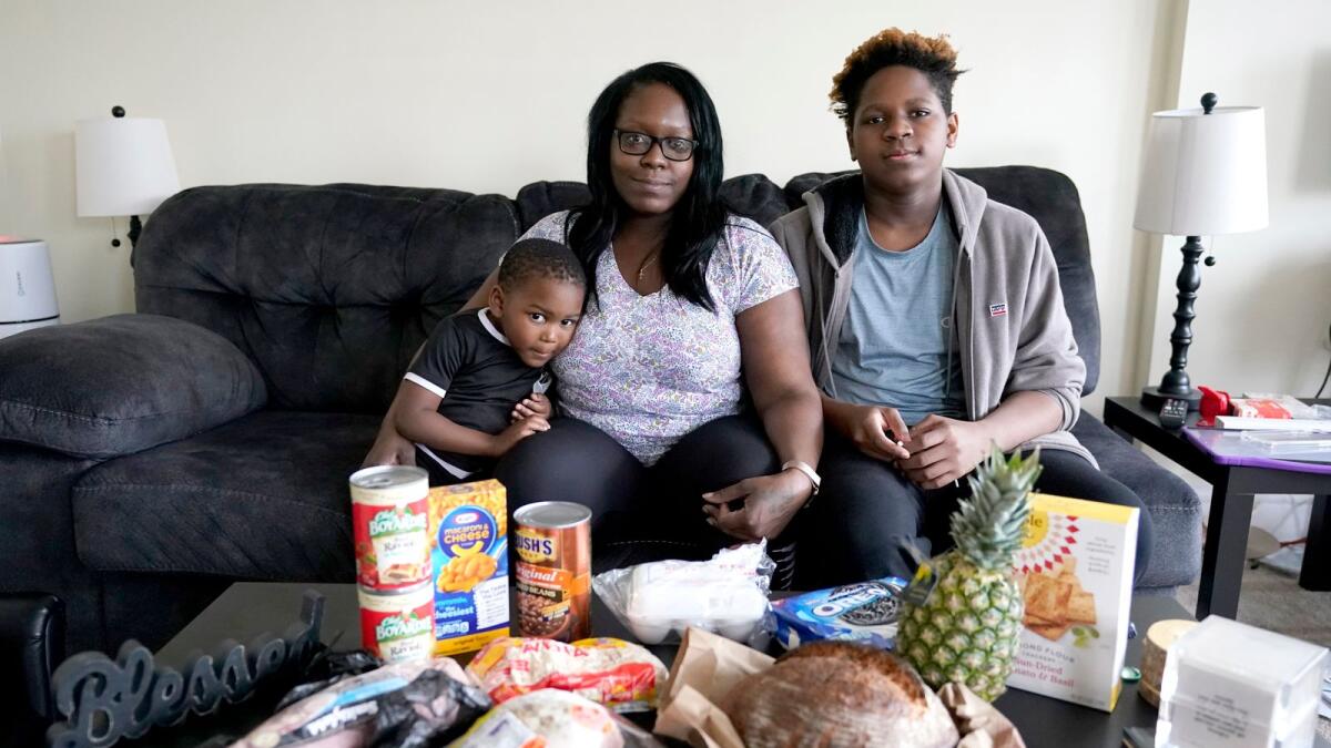 Briana Dominguez, centre, sits with her sons, Noah Scott, 4, left, and Nehemiah Powell, 14, for a portrait inside their their Skokie, Ill., apartment with groceries she received at the Hillside Food Pantry. After her employer eliminated her job, the family is moving to Georgia where living costs are lower.