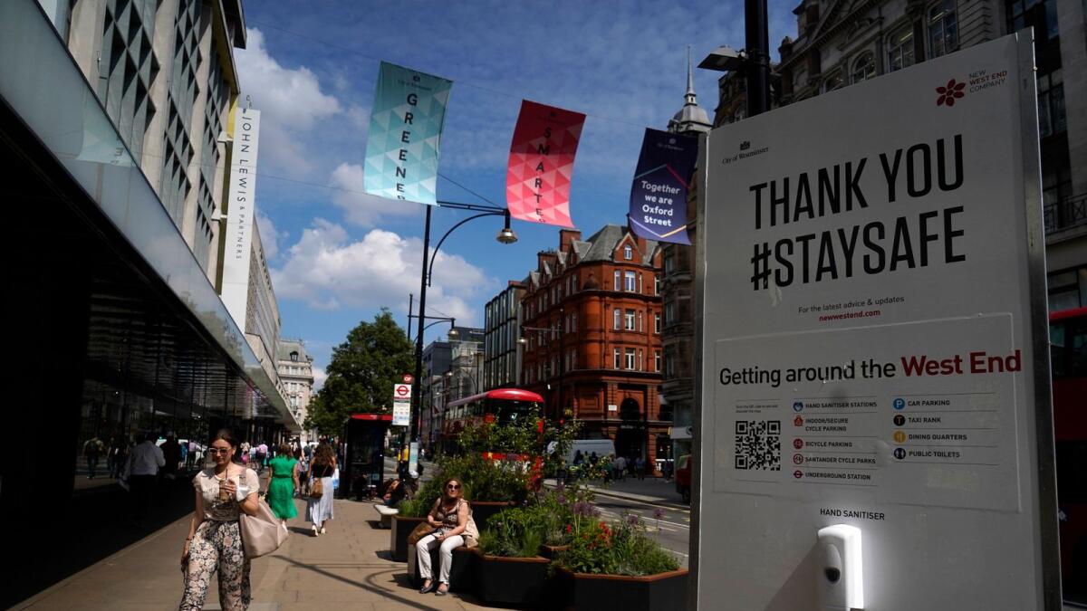 Pedestrians walk past a coronavirus information sign as they pass shops on Oxford Street. Photo: AFP