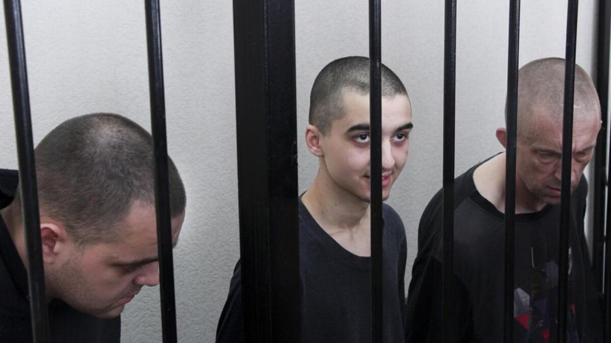 Two British citizens Aiden Aslin, left, and Shaun Pinner, right, and Moroccan Saaudun Brahim, center, sit behind bars in a courtroom in Donetsk, in the territory which is under the Government of the Donetsk People's Republic control, eastern Ukraine, Thursday, June 9, 2022. (AP Photo)