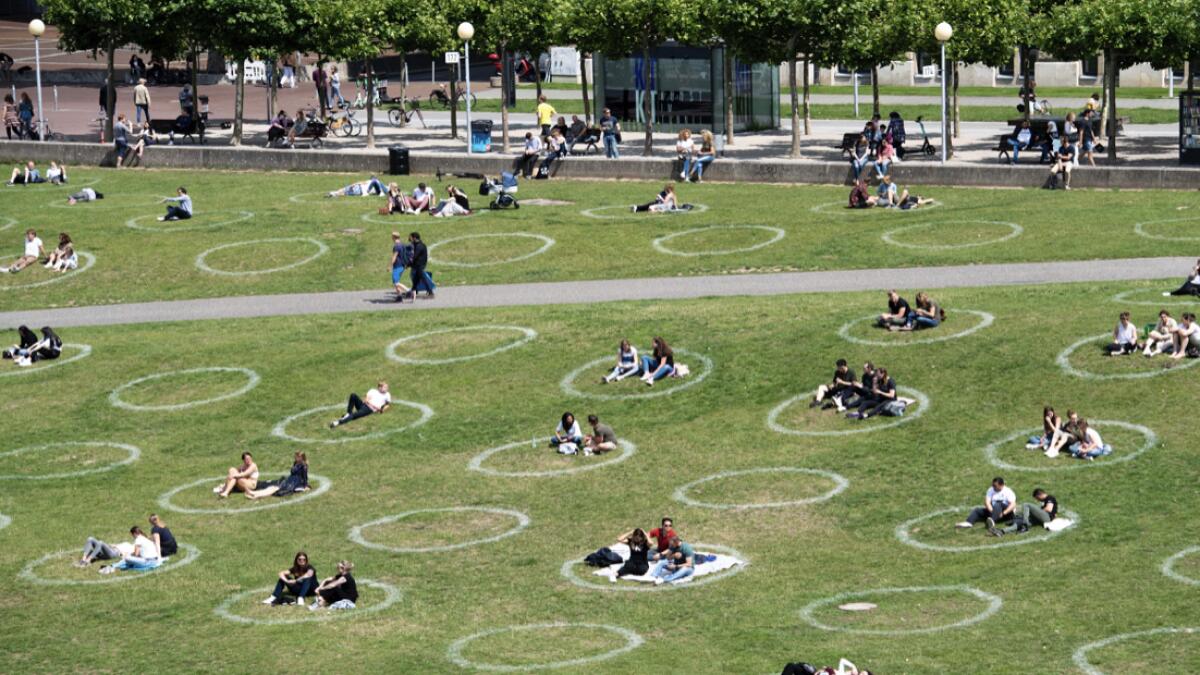 People sit in painted circles on a meadow on the banks of the Rhine in Cologne, Germany, on Saturday, July 11, 2020. The circles are to ensure that the minimum distance is maintained during the corona pandemic. AP