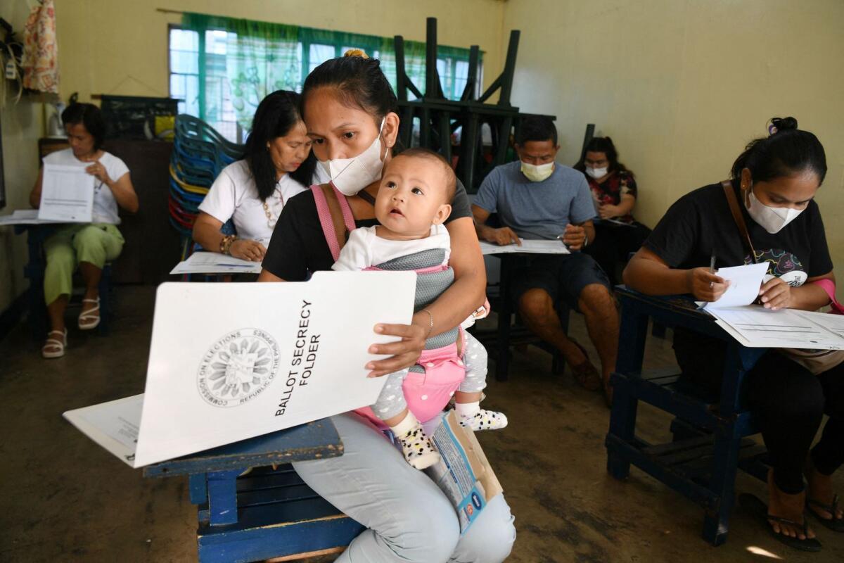 A mother holding her child goes through voting documents at a polling station for the nationwide village and youth elections in Manila on October 30, 2023.— AFP file
