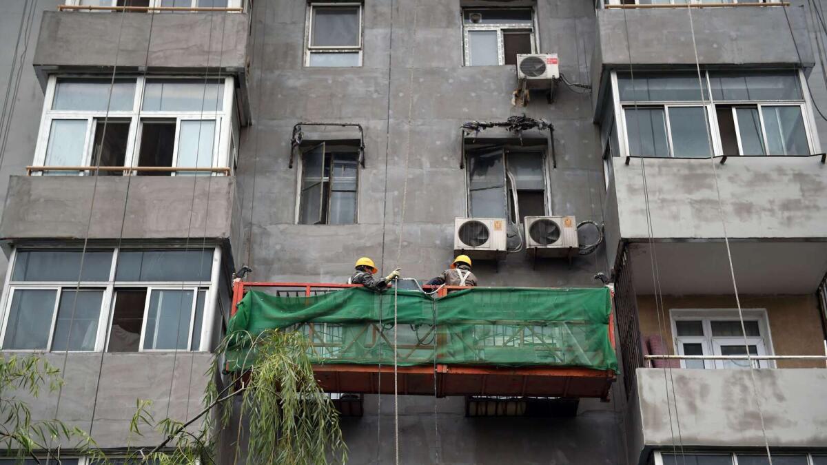 Labourers work on the exterior of an apartment building in Beijing on October 25, 2015. China's leaders will gather on October 26 to hash out a new Five Year Plan to battle slowing growth, and analysts say they must choose between chasing a traditional GDP target and embracing reforms such as to the 'one child policy' to help the country develop its full potential. AFP PHOTO / GREG BAKER