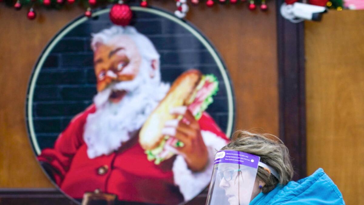 A woman wears a face shield as she walks past an image of Santa Claus at a Christmas market, in London. — AP