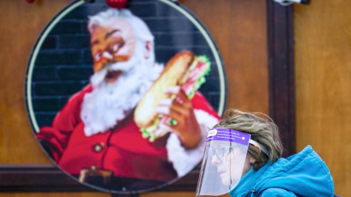 A woman wears a face shield as she walks past an image of Santa Claus at a Christmas market, in London. — AP