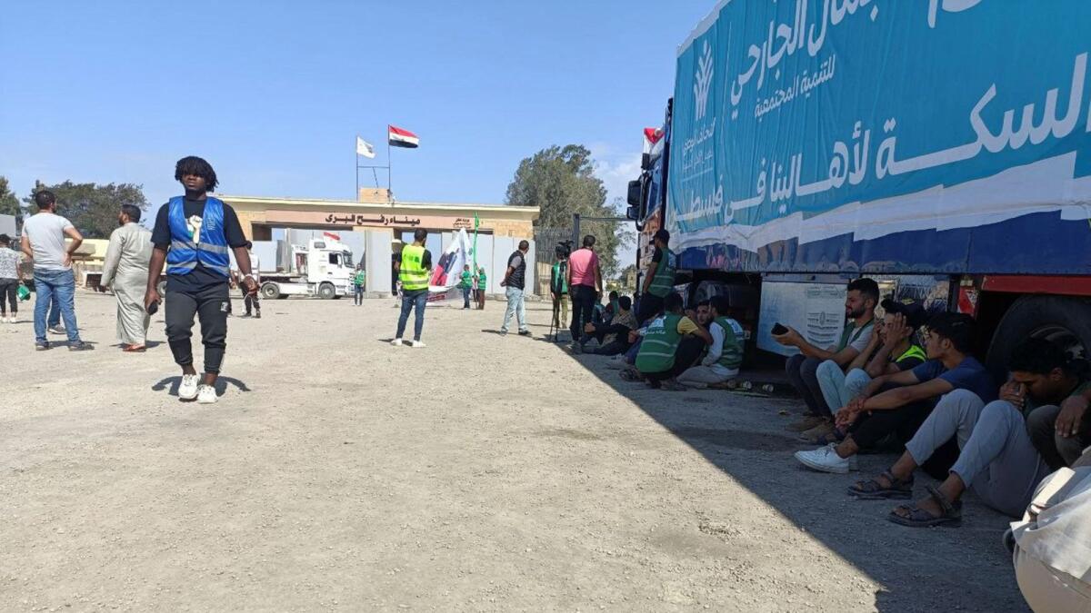 Egyptian volunteers sit on the ground next to trucks after seeing smoke rising from the Palestinian side at the Rafah crossing, as aid groups wait for the reopening of the border. — Reuters