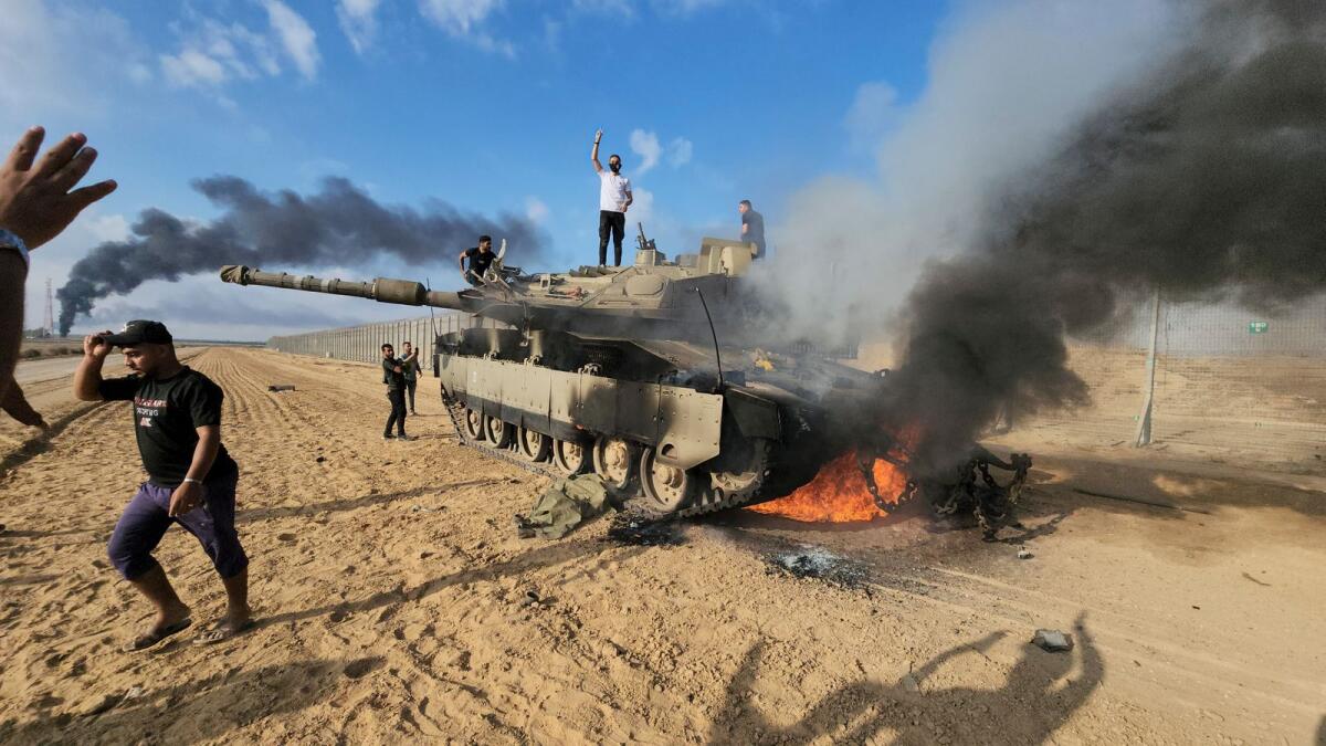 Palestinians stand on a destroyed Israeli tank at the Gaza Strip fence east of Khan Younis on Saturday, October 7, 2023. — AP