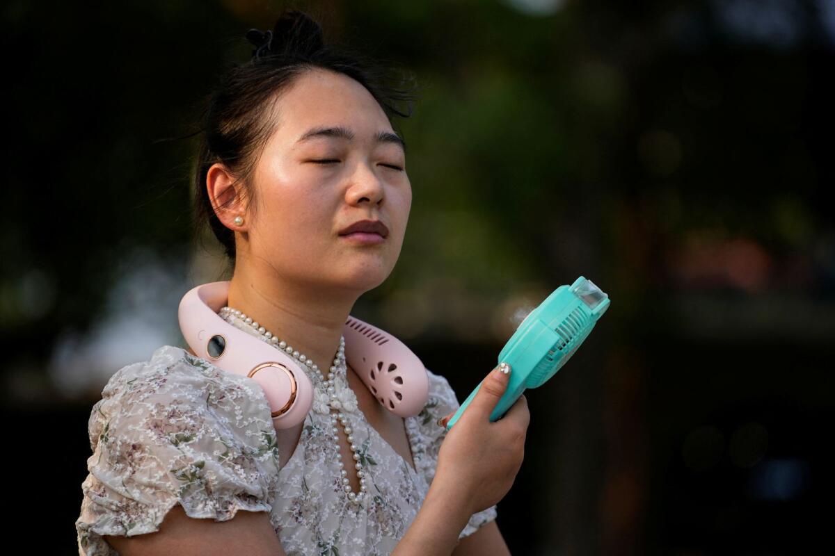 A woman uses a fan as she walks at a park amid an alert for heatwave in Shanghai, China July 12, 2023. Photo: Reuters