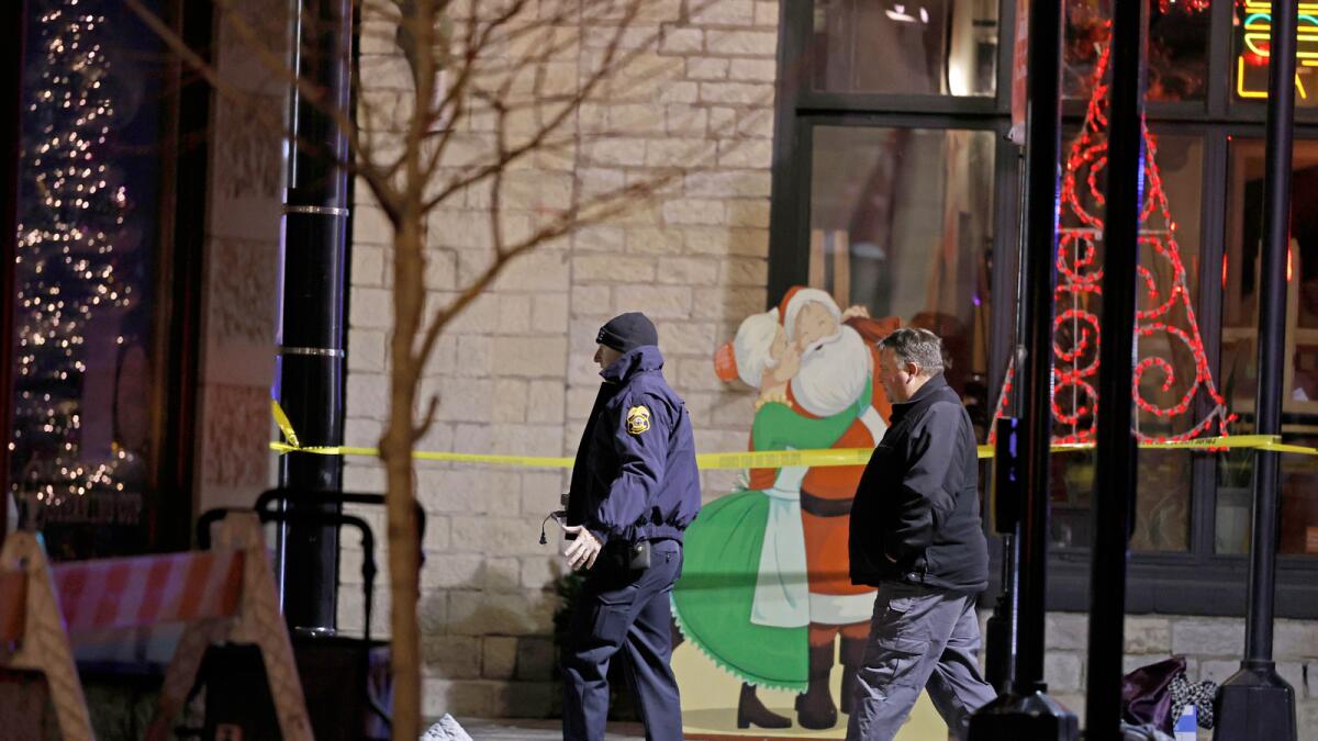 Holiday decorations can be seen in the background as police investigators in downtown Waukesha inspect the spot where a man drove through a parade. – AP