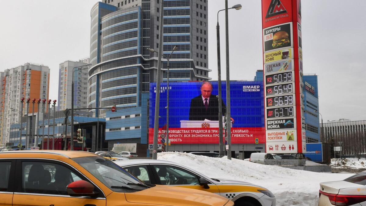 A screen displays the broadcasting of Russia's President Vladimir Putin's annual state of the nation address, on the facade of a building as cars drive past a petrol station, in Moscow. — AFP