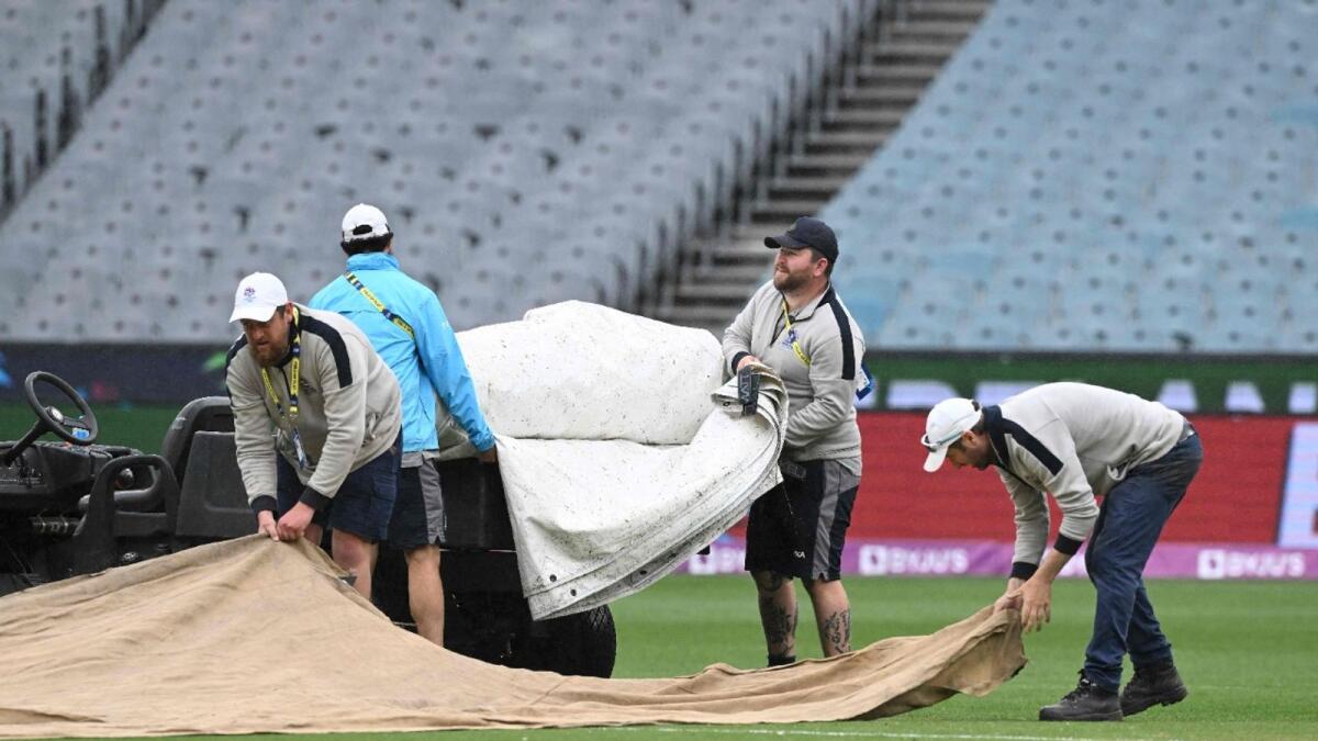 Groundmen cover the pitch area as rain delays the game between England and Ireland at the Melbourne Cricket Ground (MCG) on October 26. — AFP