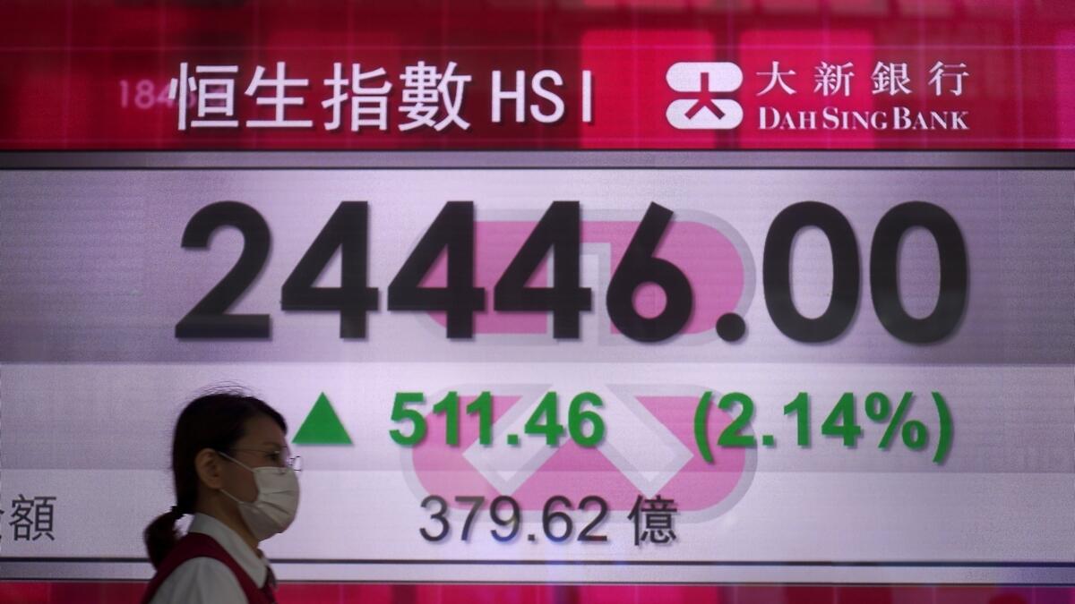 A woman wearing face mask walks past a bank electronic board showing the Hong Kong share index on Tuesday. -  AP