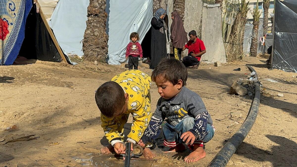 Palestinian children get water from a pipe, as displaced Palestinians who fled their houses due to Israeli strikes, shelter in a tent camp in Khan Younis. — Reuters