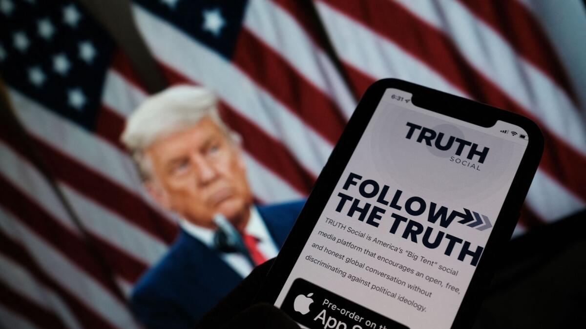 A person checking the app store on a smartphone for 'Truth Social', with a photo of former US president Donald Trump on a computer screen in the background, in Los Angeles. — AFP file photo