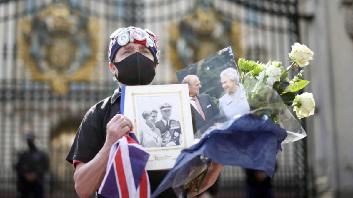 A mourner holds flowers and pictures of Britain's Queen Elizabeth II and her husband Prince Philip outside Buckingham Palace. — Reuters