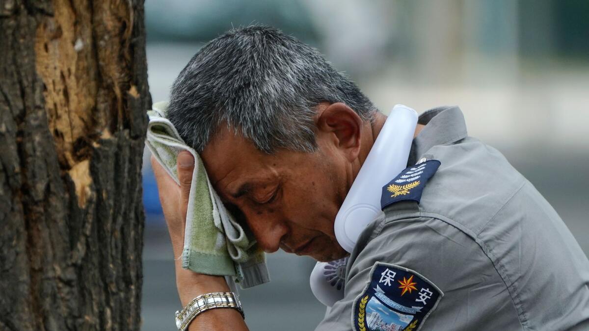 A security guard wearing an electric fan on his neck wipes his sweat on a hot day in Beijing, Monday, July 3, 2023.  – AP