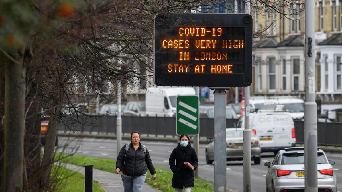 People walk past a roadside public health information sign, amidst the coronavirus disease (COVID-19) pandemic, in London, Britain, December 29, 2020.