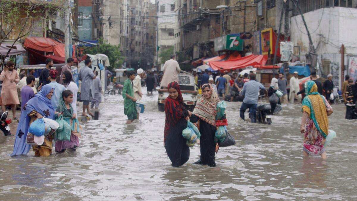 People wade through a flooded road in a business district after a heavy rainfall in Karachi. — AP