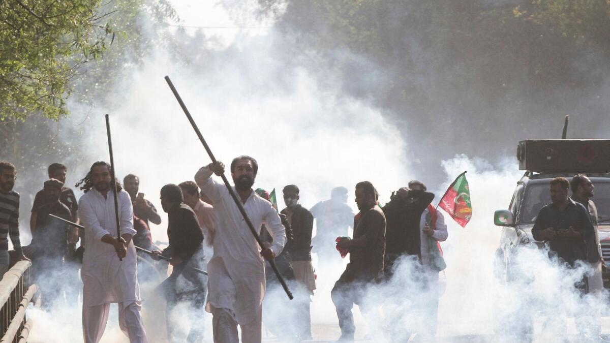 Supporters of former prime minister Imran Khan react amid tear gas fired by the police to disperse them during clashes ahead of an election campaign rally in Lahore on Wednesday. — Reuters