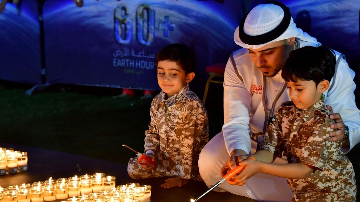 A man and two children light candles after the building lights were switched off for the Earth Hour environmental campaign in Dubai on March 24, 2018.