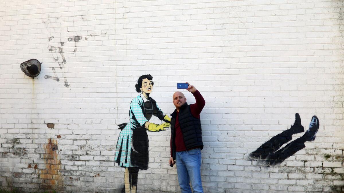 A man takes a selfie with an artwork depicting violence against women, painted by street artist Banksy for the occasion of Valentines Day on a residential street in Margate, Kent, Britain, Tuesday. — Reuters