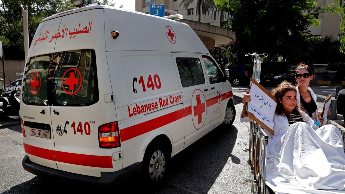 A pharmacist sits on a stretcher by an ambulance holding a sign reading in Arabic 'no gasoline = no ambulance' as people protest in Beirut. Photo: AFP