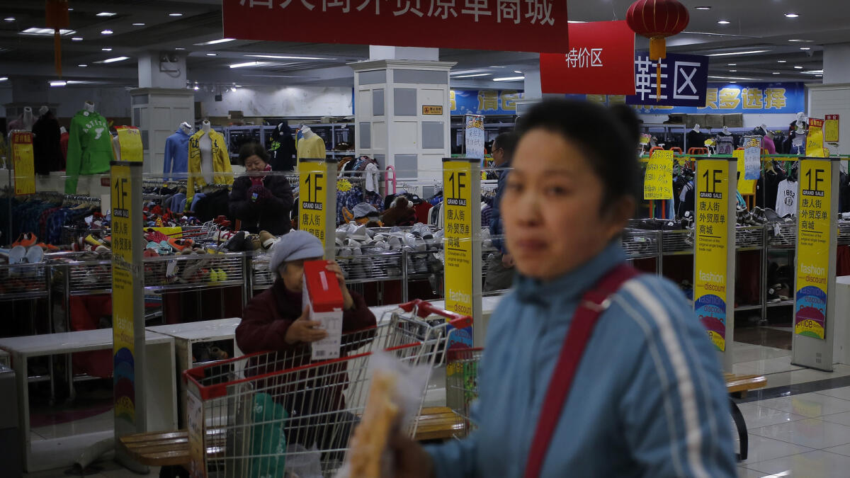 A woman with her groceries walks past people shop at a Chinatown foreign trade mall in Beijing, Tuesday, March 1, 2016. China's manufacturing lost momentum again last month, according to two surveys of factory activity released Tuesday that highlighted sluggish conditions in the world's second biggest economy. (AP Photo/Andy Wong)