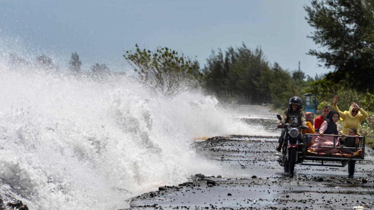 People riding a rickshaw react as a large wave breaks over the wall hitting a street on the shores of Banda Aceh. Photo: AFP