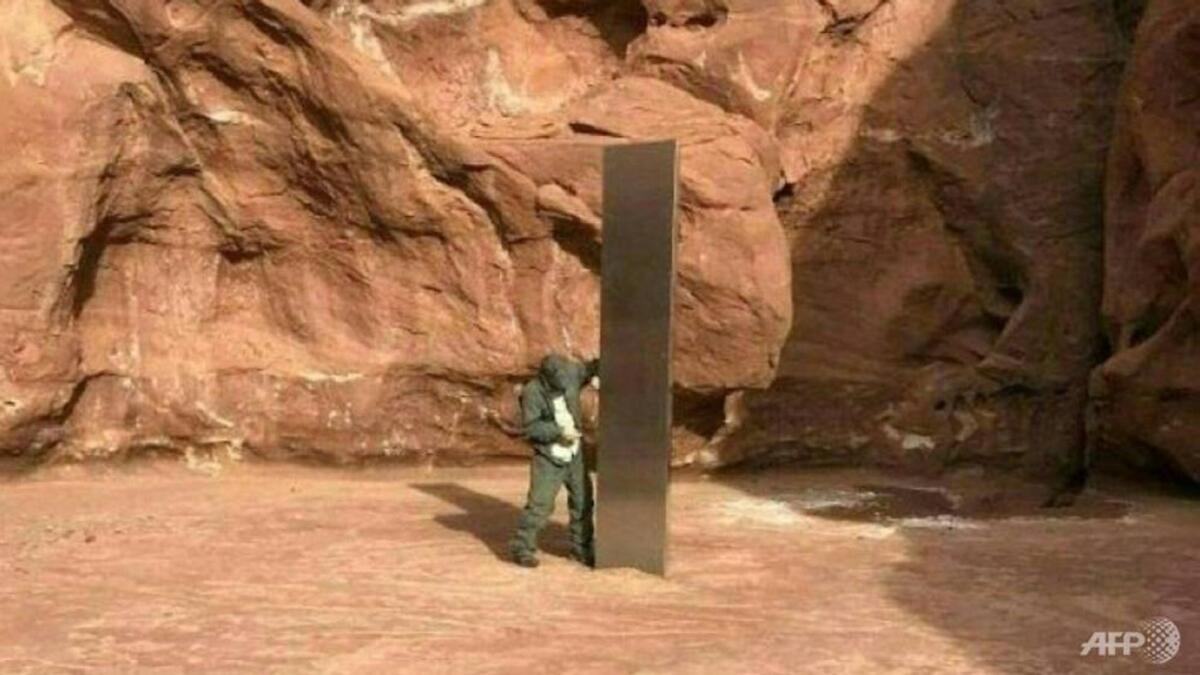 A Utah state worker inspecting a metal monolith that was found installed in the ground in a remote area of red rock in Utah.