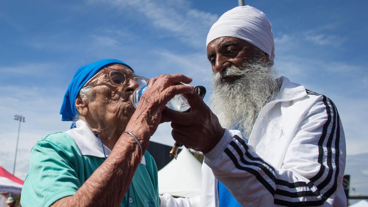 Man Kaur, left, 100, of India, is helped by her son Gurdev Singh, 78, as she takes a drink of water after competing in the 100-meter track and field event at the Americas Masters Games in Vancouver, British Columbia, Monday, Aug. 29, 2016. (Darryl Dyck/The Canadian Press via AP)