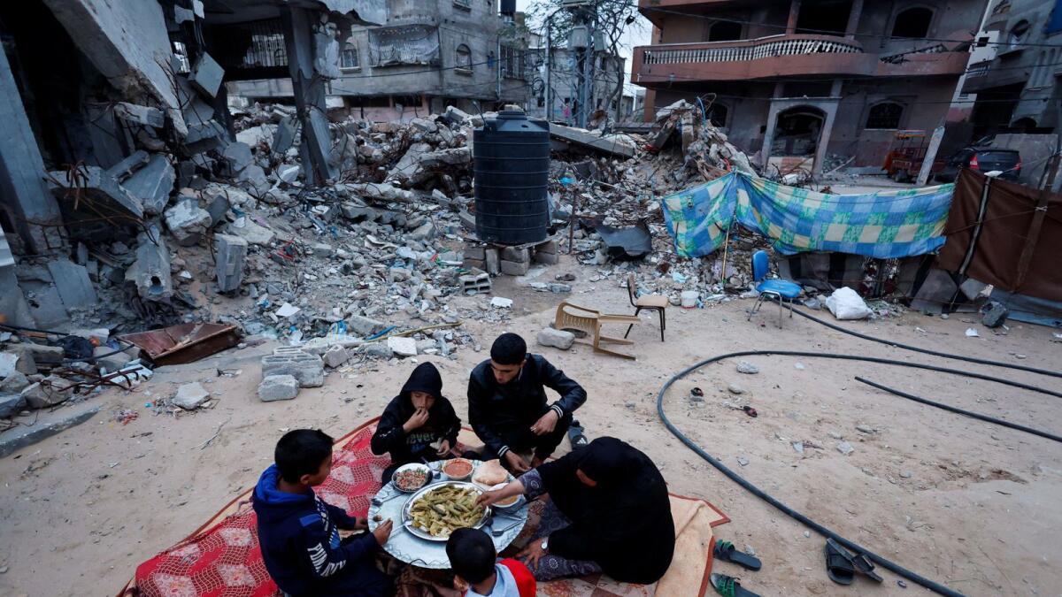 Members of Palestinian Abu Ghouta family eat their iftar meal as they break their fast near the rubble of their destroyed house in Rafah. — Reuters