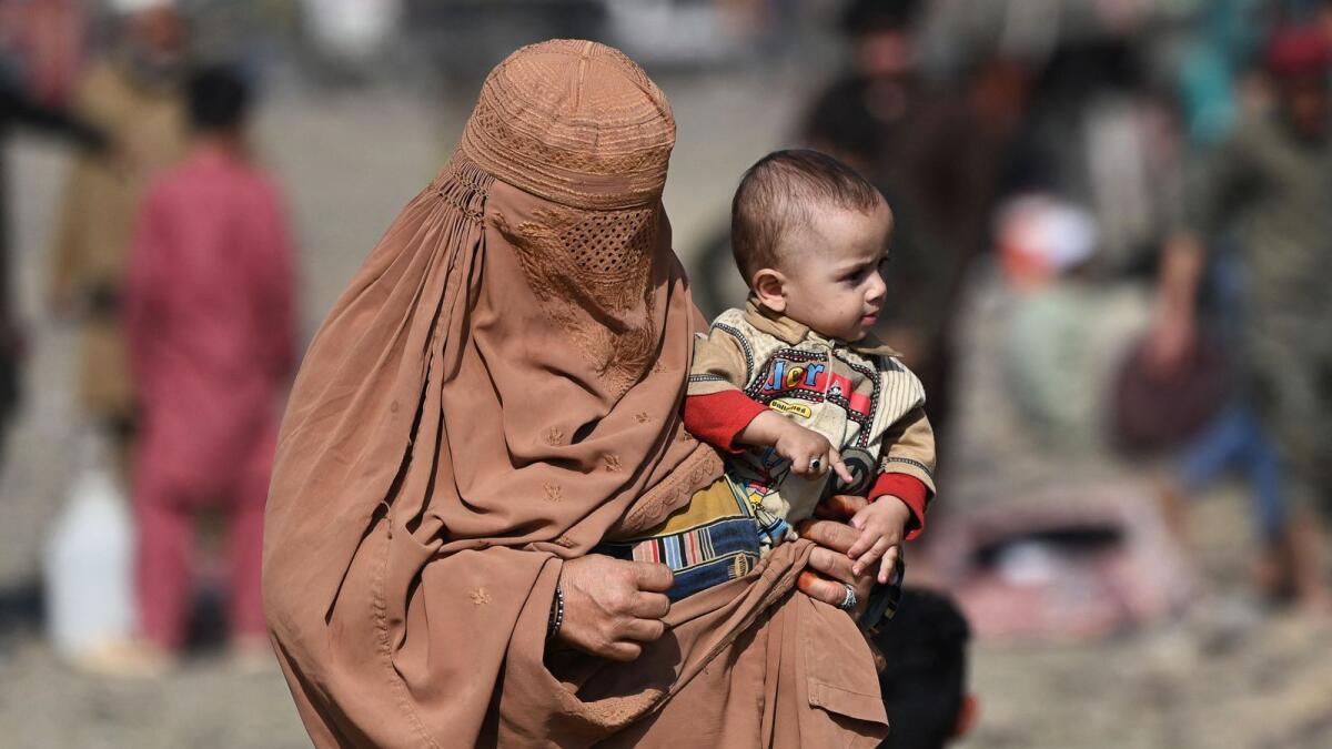 TOPSHOT - An Afghan refugee with her child who arrived from Pakistan walk at a makeshift camp near the Afghanistan-Pakistan Torkham border in Nangarhar province on November 2, 2023. More than 165,000 Afghans have fled Pakistan since Islamabad issued an ultimatum to 1.7 million people a month ago to leave or face arrest and deportation, officials said on November 2. (Photo by Wakil KOHSAR / AFP)