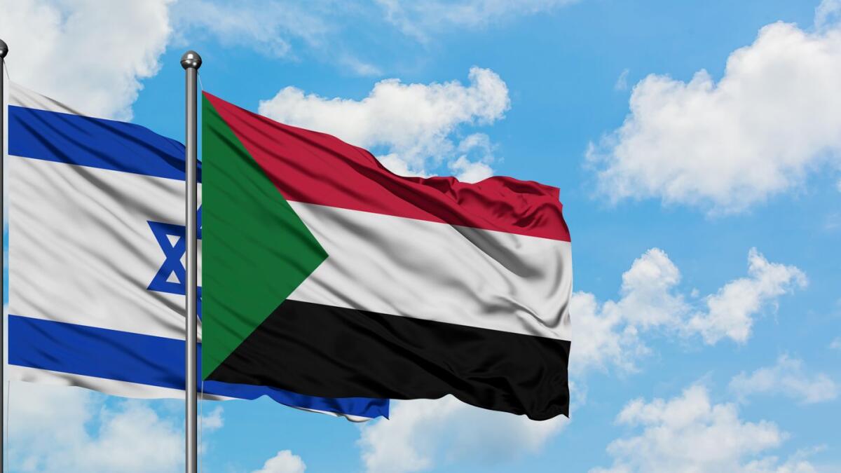 Israel and Sudan flag waving in the wind against white cloudy blue sky together.