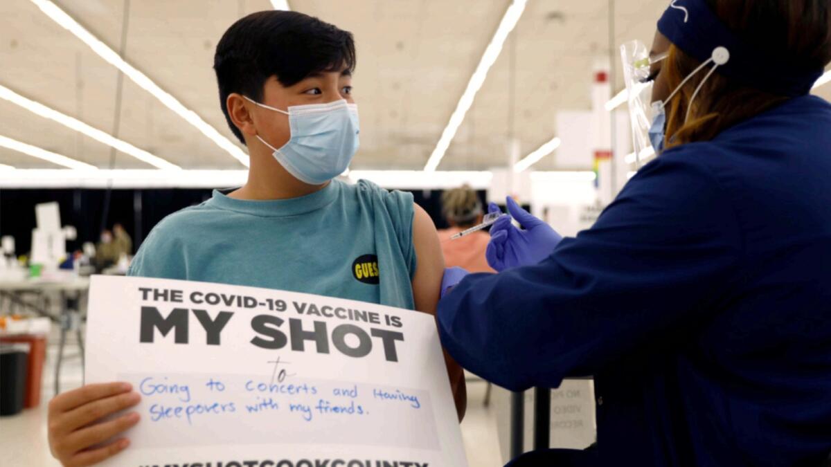 Lucas Kittikamron-Mora, 13, holds a sign in support of Covid-19 vaccinations as he receives his first Pfizer vaccination at the Cook County Public Health Department. — AP