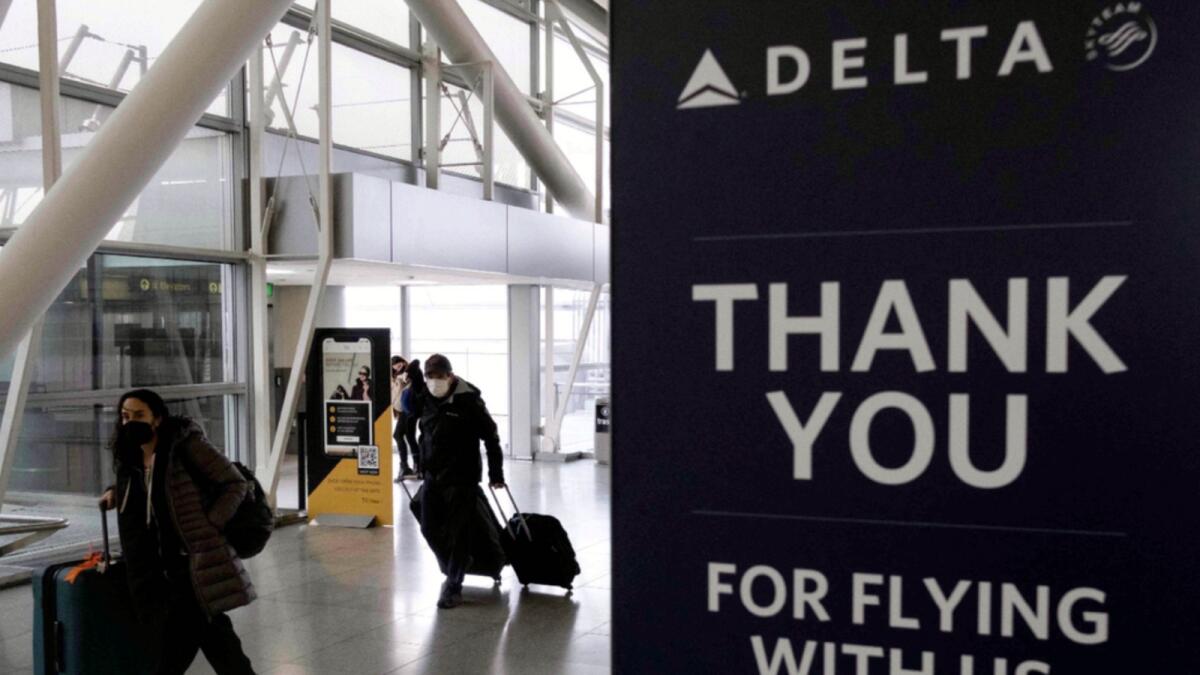 Travellers carrying suitcases walk past a sign of Delta Airlines at John F. Kennedy International Airport in New York. — AFP