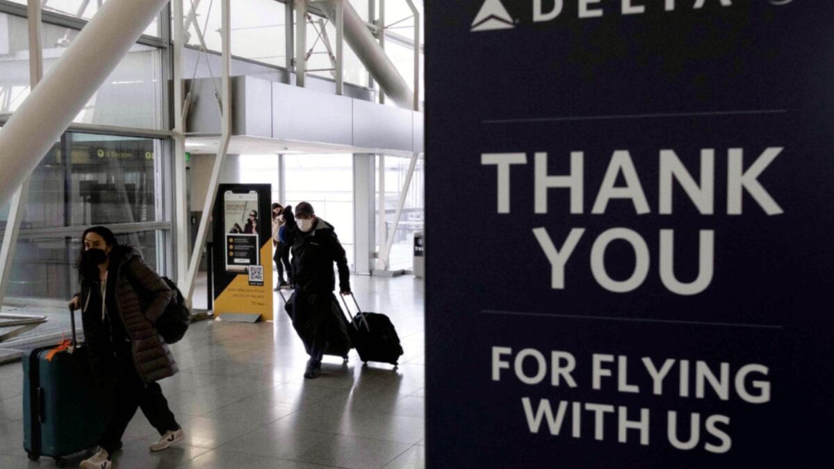 Travellers carrying suitcases walk past a sign of Delta Airlines at John F. Kennedy International Airport in New York. — AFP