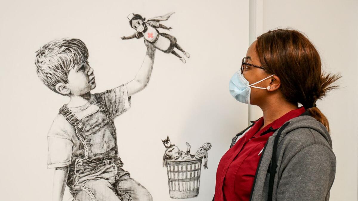 A member of staff posing with an artwork by street artist Banksy called 'Game Changer' as a tribute to NHS staff who are continuing to work during the Covid-19 pandemic, on a wall at the University Hospital Southampton,  England. Photo: AFP