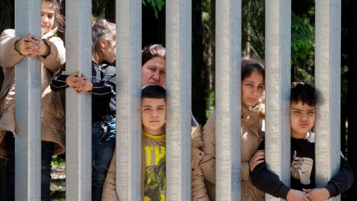 Members of a group of some 30 migrants seeking asylum are seen in Bialowieza, Poland, on Sunday across a wall that Poland has built on its border with Belarus to stop massive migrant pressure. — AP